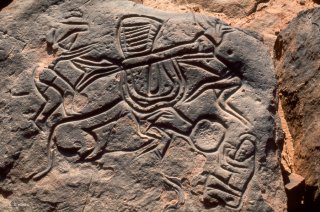 Gravure rupestre. Deux personnages chargent du matériel sur les cornes d'un bovin, un autre lui donne à manger dans une auge.